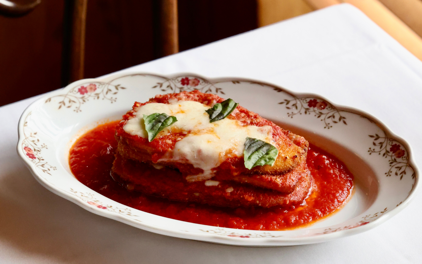 Layers of crispy eggplant parmesan with melted mozzarella, fresh basil, and tomato sauce on a vintage floral plate
