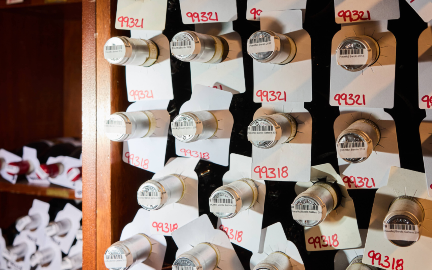 Rows of Barolo wine bottles stored horizontally in Babbo's cellar, labeled with handwritten inventory numbers