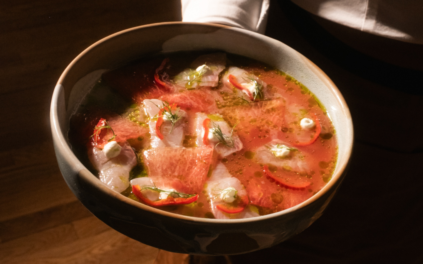 Delicate fish crudo with red chili, fresh dill, herb oil, and whipped cream garnish served in a handcrafted ceramic bowl at Upland